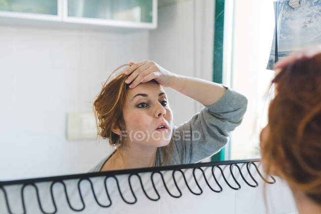 Відображення молодої жінки з рукою на лобі, дивлячись на дзеркало у ванній кімнаті — стокове фото