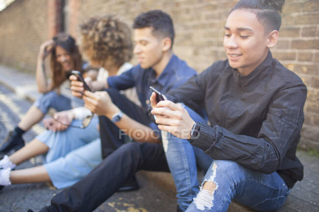 Four friends sitting in street, looking at smartphones — Stock Photo