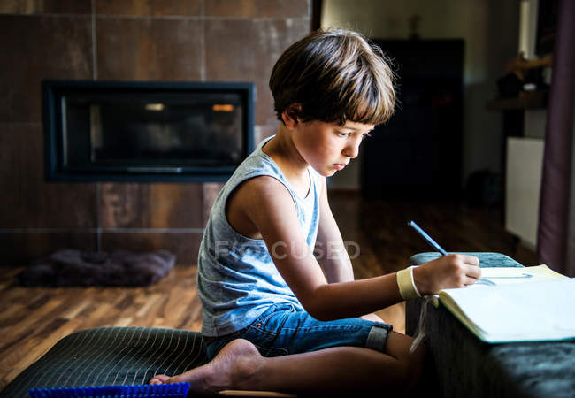 Хлопчик на колінах на підлозі малює в робочій книзі — стокове фото
