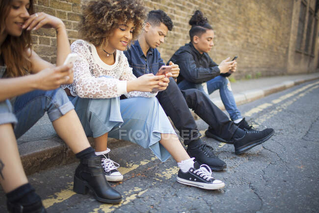 Quattro amici seduti in strada, a guardare gli smartphone — Foto stock