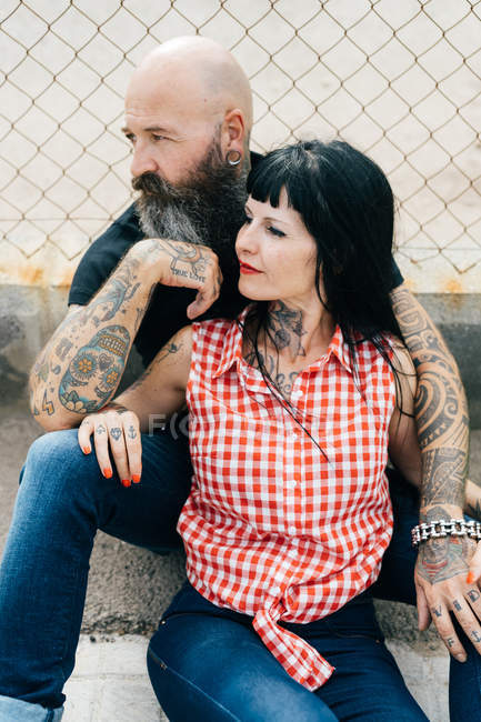 Mature tattooed hipster couple sitting on wall — Stock Photo