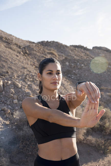 Jovem corredor do sexo feminino esticando os braços na paisagem árida — Fotografia de Stock