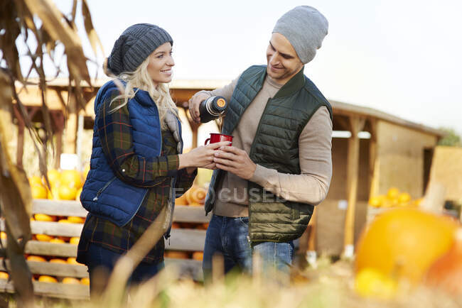 Couple pouring coffee from flask at pumpkin patch — Stock Photo