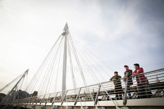 Drei Freunde, die auf einer Brücke stehen und die Aussicht betrachten, Golden Jubilee Footbridge, London, England, UK — Stockfoto