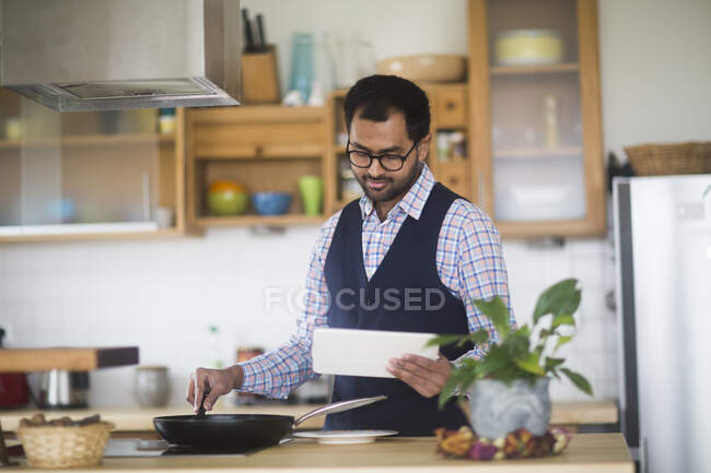 Чоловік готує їжу під час використання цифрового планшета вдома — стокове фото