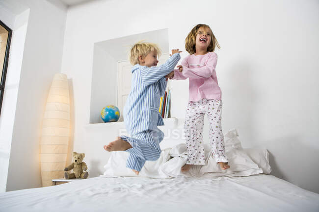 Female and male twins jumping together on bed — Stock Photo