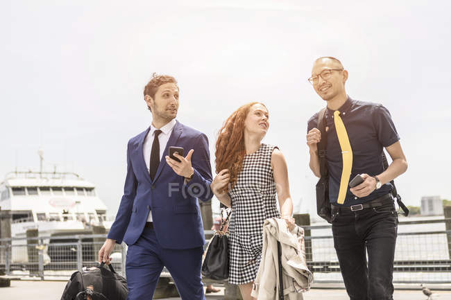 Businessmen and woman walking and talking on waterfront — Stock Photo