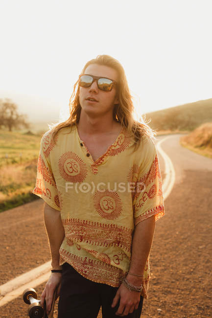 Портрет длинноволосого молодого скейтбордиста на сельской дороге, Эксетер, Калифорния, США — стоковое фото