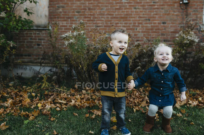 Happy male and female toddler twins holding hands in garden — Stock Photo