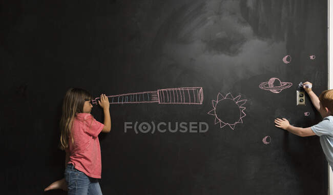 Menina olhando através de telescópio imaginário desenhado em quadro negro — Fotografia de Stock
