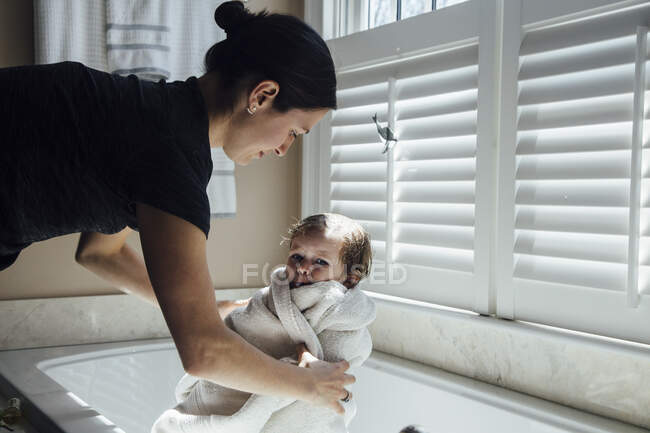 Мать вытаскивает дочь из ванны завернутую в полотенце — стоковое фото