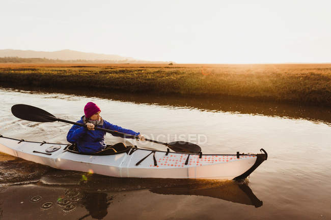 Mujer adulta haciendo kayak en el río al atardecer, Morro Bay, California, EE.UU. - foto de stock
