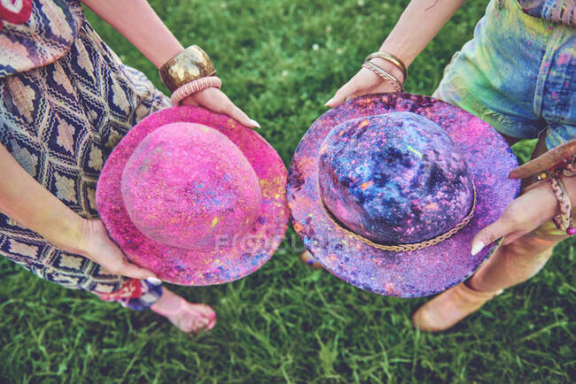 Waist down view of two young women holding felt hats covered in coloured chalk at festival — Stock Photo
