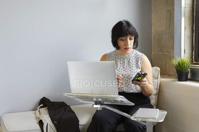 Mujer de negocios utilizando el ordenador portátil y la celebración de teléfonos inteligentes - foto de stock