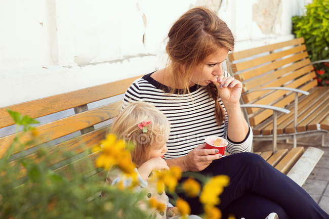 Mãe e filha de criança comendo sorvete no banco do parque — Fotografia de Stock
