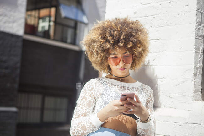 Junge Frau im Freien, an Wand gelehnt, Smartphone im Blick — Stockfoto