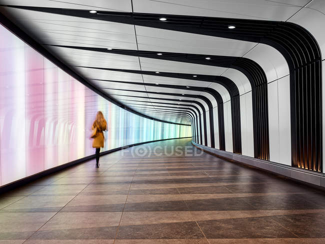 Вид сзади женщины, идущей по пешеходной дорожке туннеля, Аэропорт Лондон-Сити, Лондон, Великобритания — стоковое фото