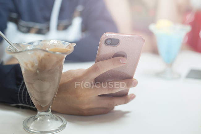 Крупним планом смартфон в руці молодого чоловіка, що сидить в їдальні — стокове фото
