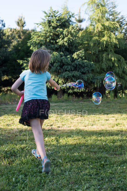 Young girl playing with bubble wand in garden, rear view — Stock Photo