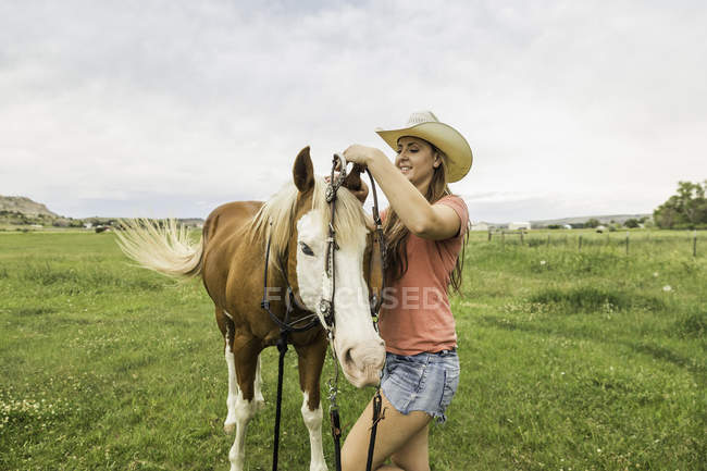 Молода жінка, поклавши вуздечку кінь ранчо поля, Bridger, штат Монтана, США — стокове фото