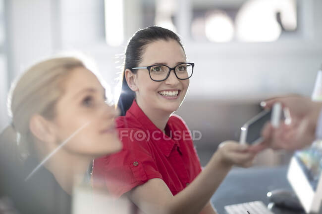 Young female office worker sharing smartphone with colleague — Stock Photo