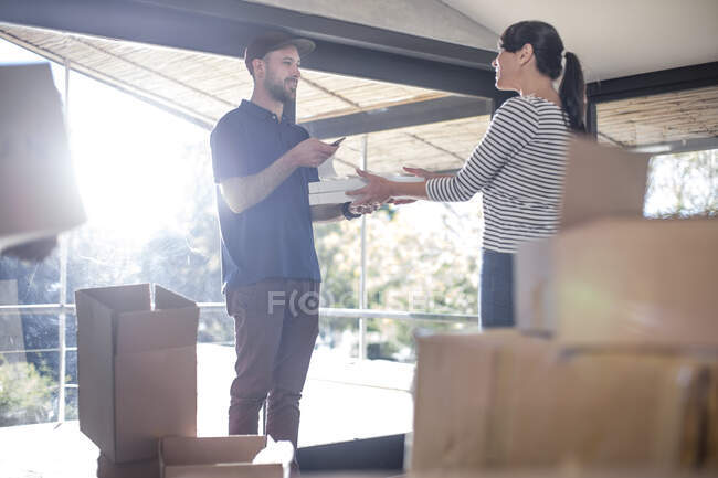 Delivery man  passing parcel to women standing in new home — Stock Photo