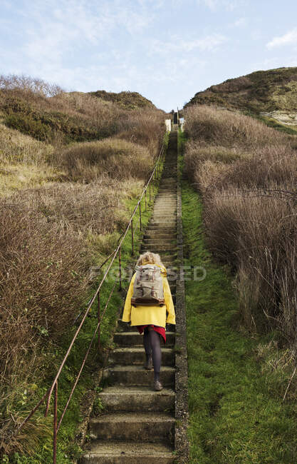 Girl with retro backpack moving up stairway near former NATO fuel station on Normandy coast — Stock Photo