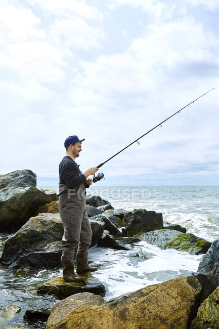 Giovane uomo in piedi su roccia e pesca — Foto stock