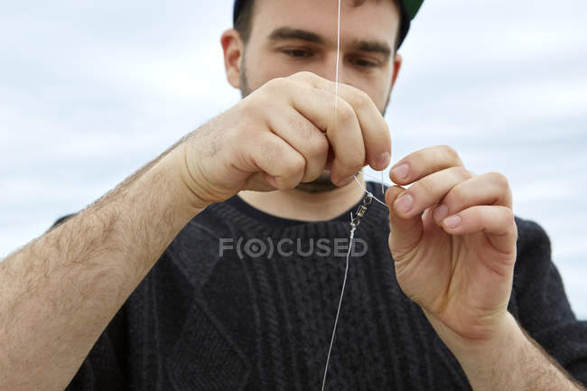 Молодой человек прикрепляет рыболовный крючок к леске — стоковое фото