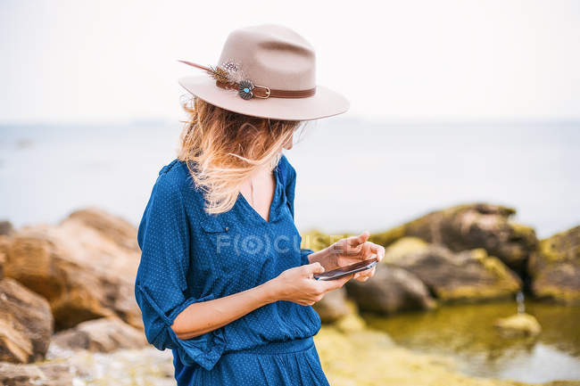 Mulher em ambiente costeiro olhando para o smartphone — Fotografia de Stock