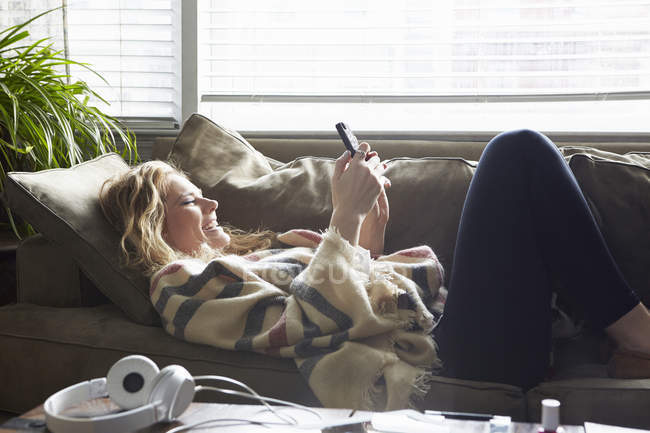 Frau benutzt Handy auf Sofa — Stockfoto