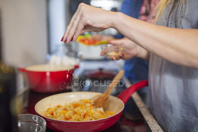 Frau in Küche würzt Essen in Pfanne — Stockfoto