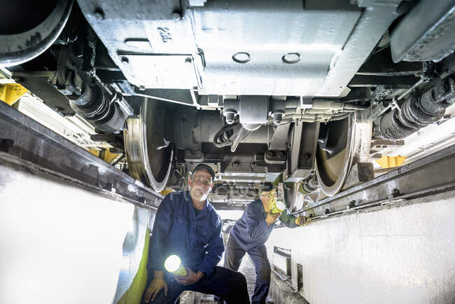 Ingenieros de locomotoras inspeccionan la parte inferior de la locomotora en obras de tren - foto de stock