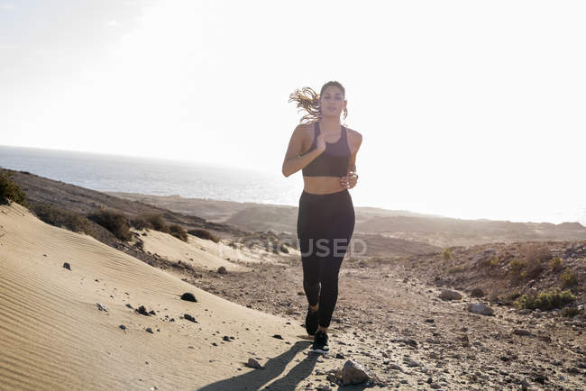 Jovem fêmea correndo em paisagem costeira árida — Fotografia de Stock