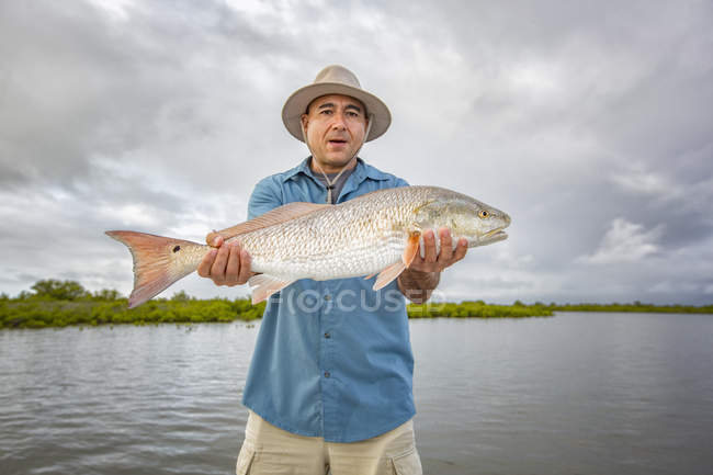 Вид спереду Чоловік тримає величезну червону рибу на відкритому повітрі — стокове фото