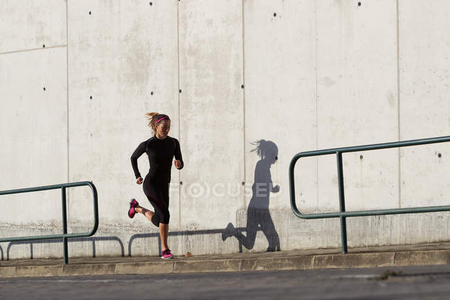 Jeune femme jogging à côté du mur en béton — Photo de stock
