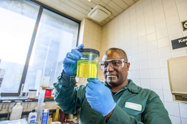 Лаборант рассматривает стакан желтого биотоплива в лаборатории биотопливного завода — стоковое фото
