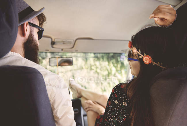 Vista sobre el hombro de una joven pareja boho con pies en furgoneta recreativa - foto de stock