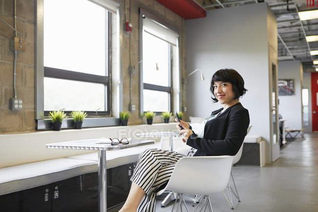 Retrato de mulher de negócios sentada à mesa no escritório com smartphone — Fotografia de Stock