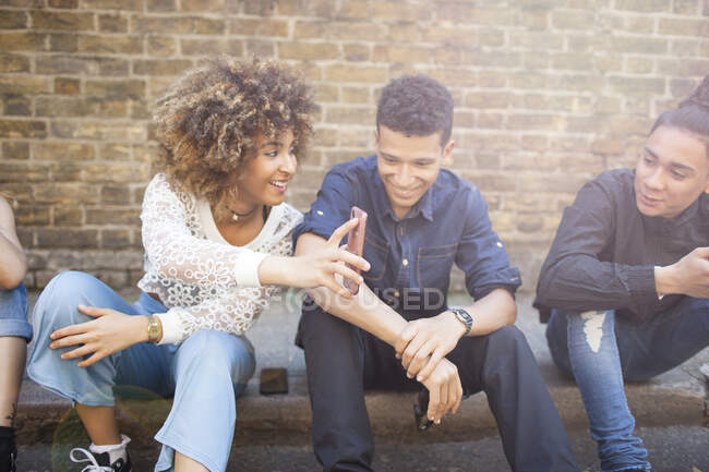 Quattro amici seduti in strada, ridendo, giovane donna in possesso di smartphone — Foto stock