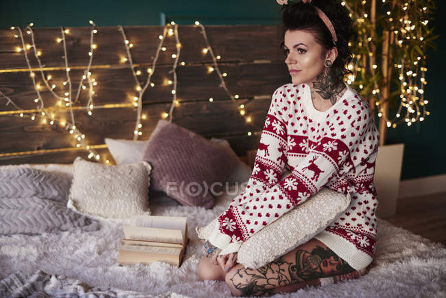 Young woman in christmas jumper sitting on bed — Stock Photo