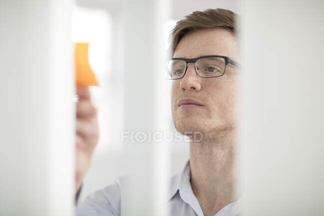 Young male office worker sticking adhesive note up in office — Stock Photo