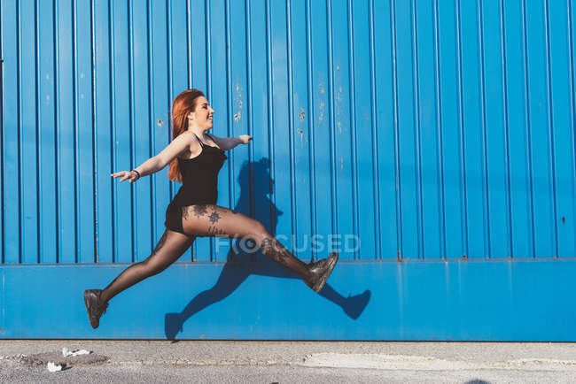 Жінка перед синьою стіною стрибає в повітрі — стокове фото