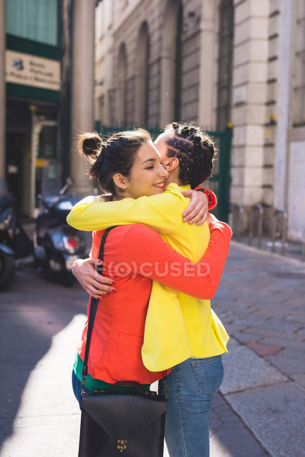 Mujeres jóvenes abrazándose en la calle, Milán, Italia - foto de stock