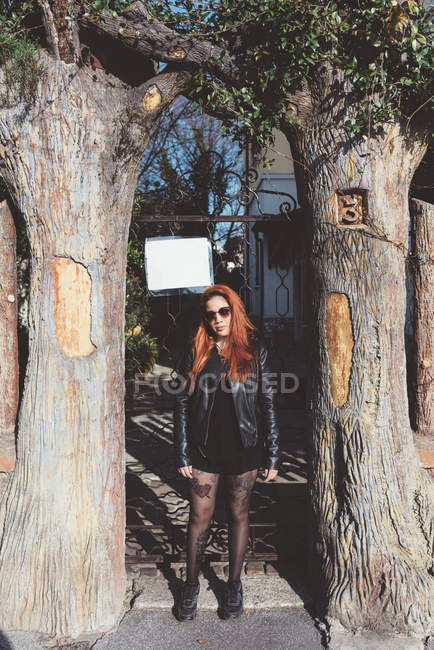Retrato de mujer pelirroja en gafas de sol de pie entre árboles - foto de stock