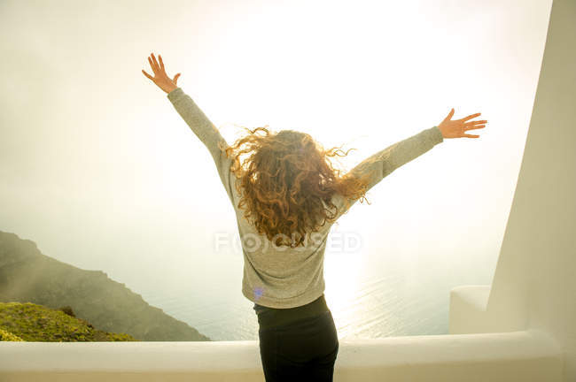 Vista posteriore della ragazza con le braccia aperte guardando il mare, Santorini, Kikladhes, Grecia — Foto stock