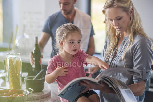Madre e hija mirando en el libro en la cocina - foto de stock