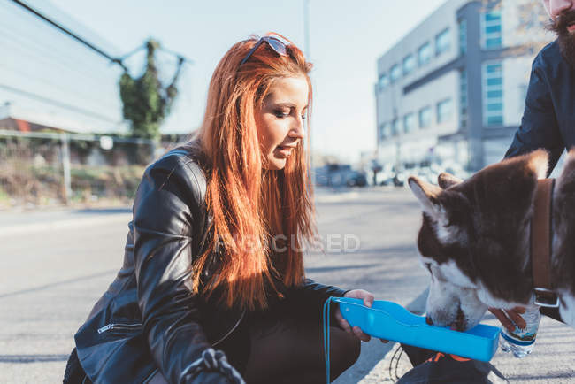 Mujer pelirroja dando bebida de agua al perro - foto de stock