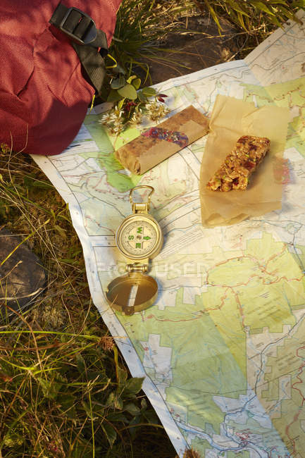 Close up of compass with map and energy bar lying on grass — Stock Photo