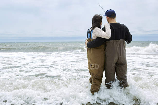 Vista trasera de pareja joven en vadeadores pescando en el mar - foto de stock